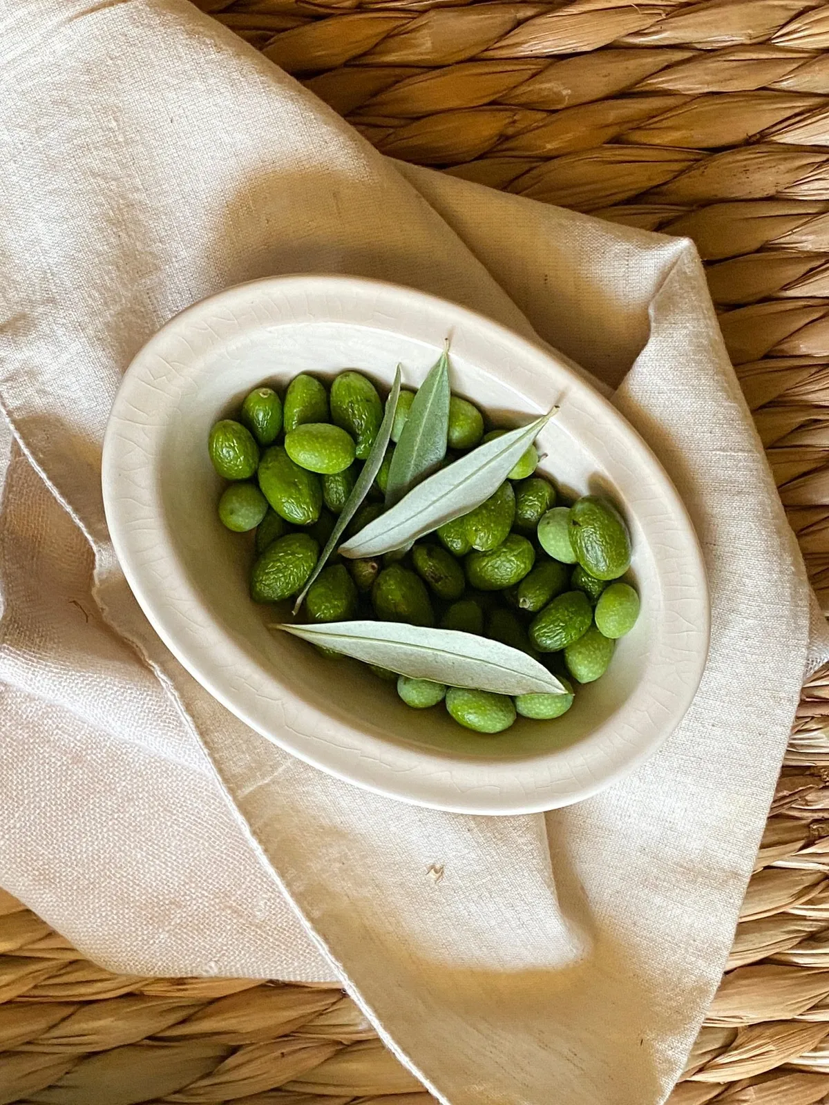 A bowl of green olives on linen