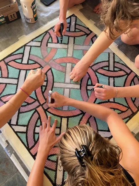 Many hands placing tiles in an interlace mosaic