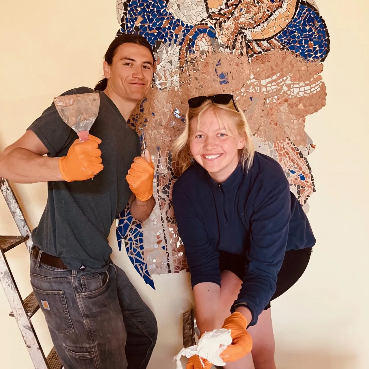 Two volunteers in front of a finished mosaic figure
