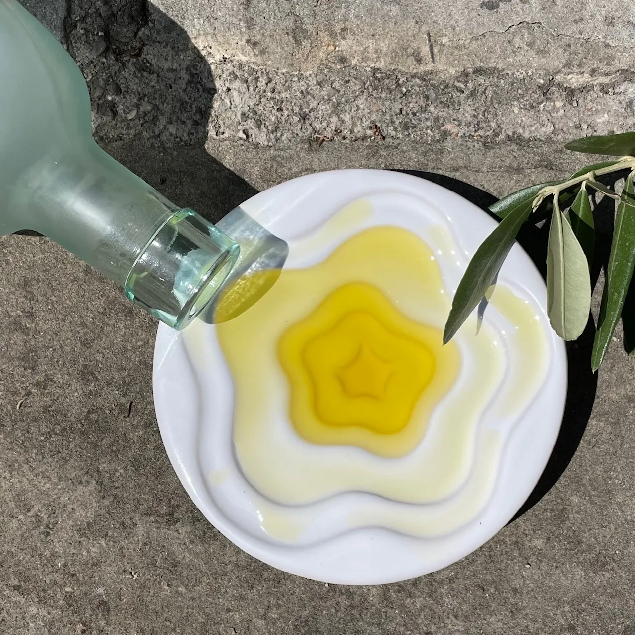 Fresh olive oil poured onto a white dish beside an olive sprig